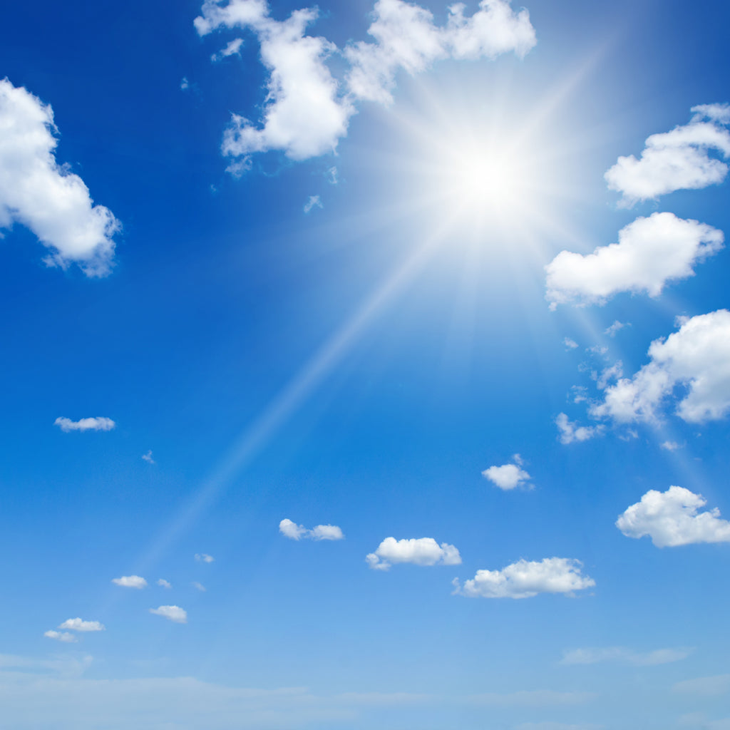 Bright summer sun shining in a clear blue sky with white clouds, representing the need for effective strategies to prepare warehouses for summer efficiency.