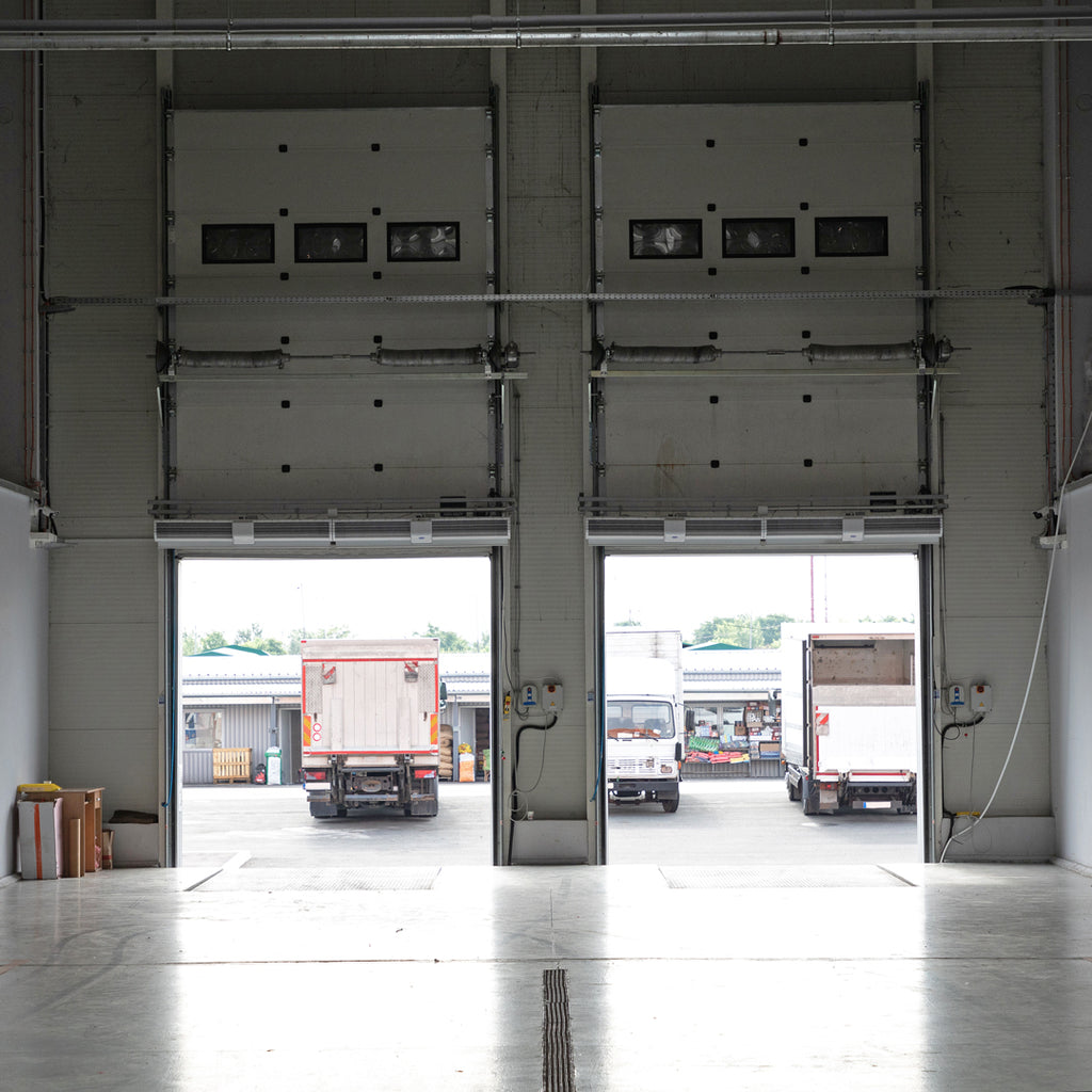 Loading docks in a warehouse with trucks, demonstrating the energy-saving potential of strip curtains in maintaining internal temperatures.