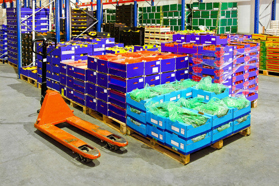 A warehouse with pallets of fresh produce in crates and pallet jacks, highlighting cold storage and food handling efficiency.