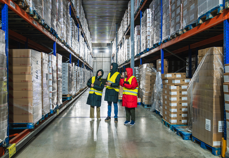Warehouse staff wearing hi-vis jackets inspecting stock inside a large distribution warehouse during winter.