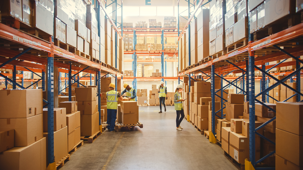 Warehouse aisle with pallet racking and boxed stock; workers in hi-vis managing inventory and picking in a busy storage area.