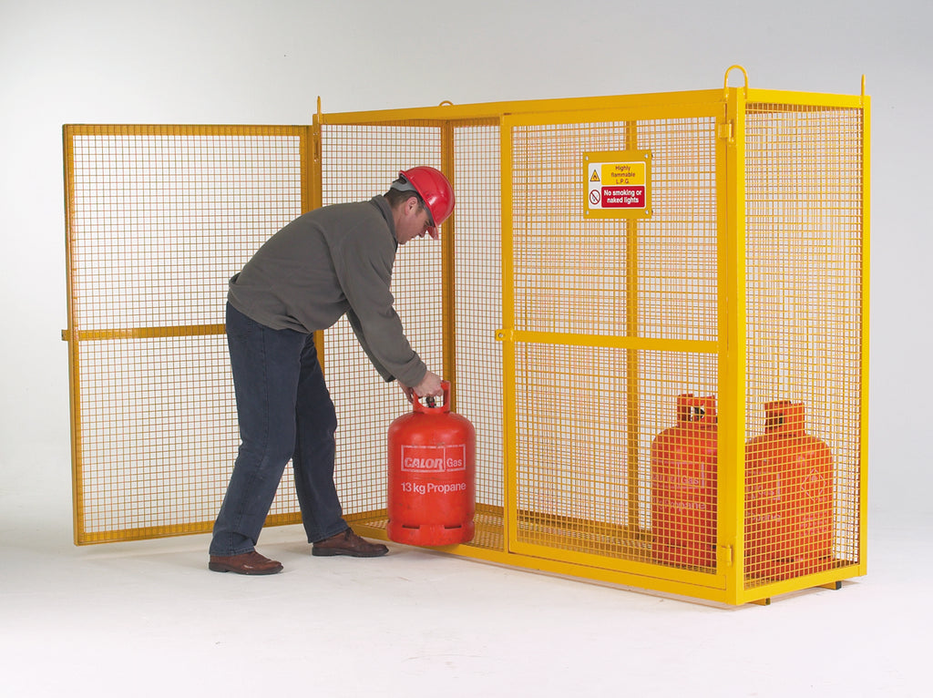 A person is placing a red gas cylinder into a yellow galvanised security cage with a mesh door.